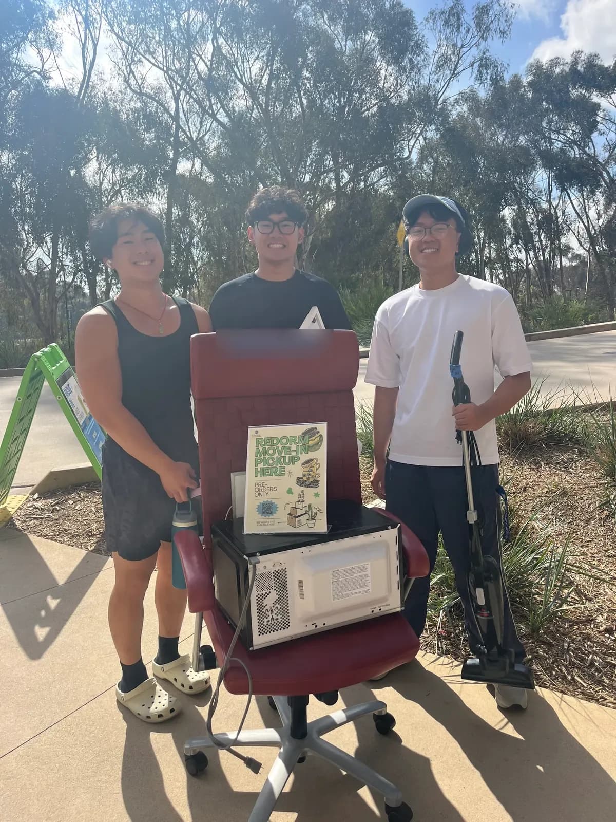 Three students at pickup with a desk chair, a microwave and a vacuum