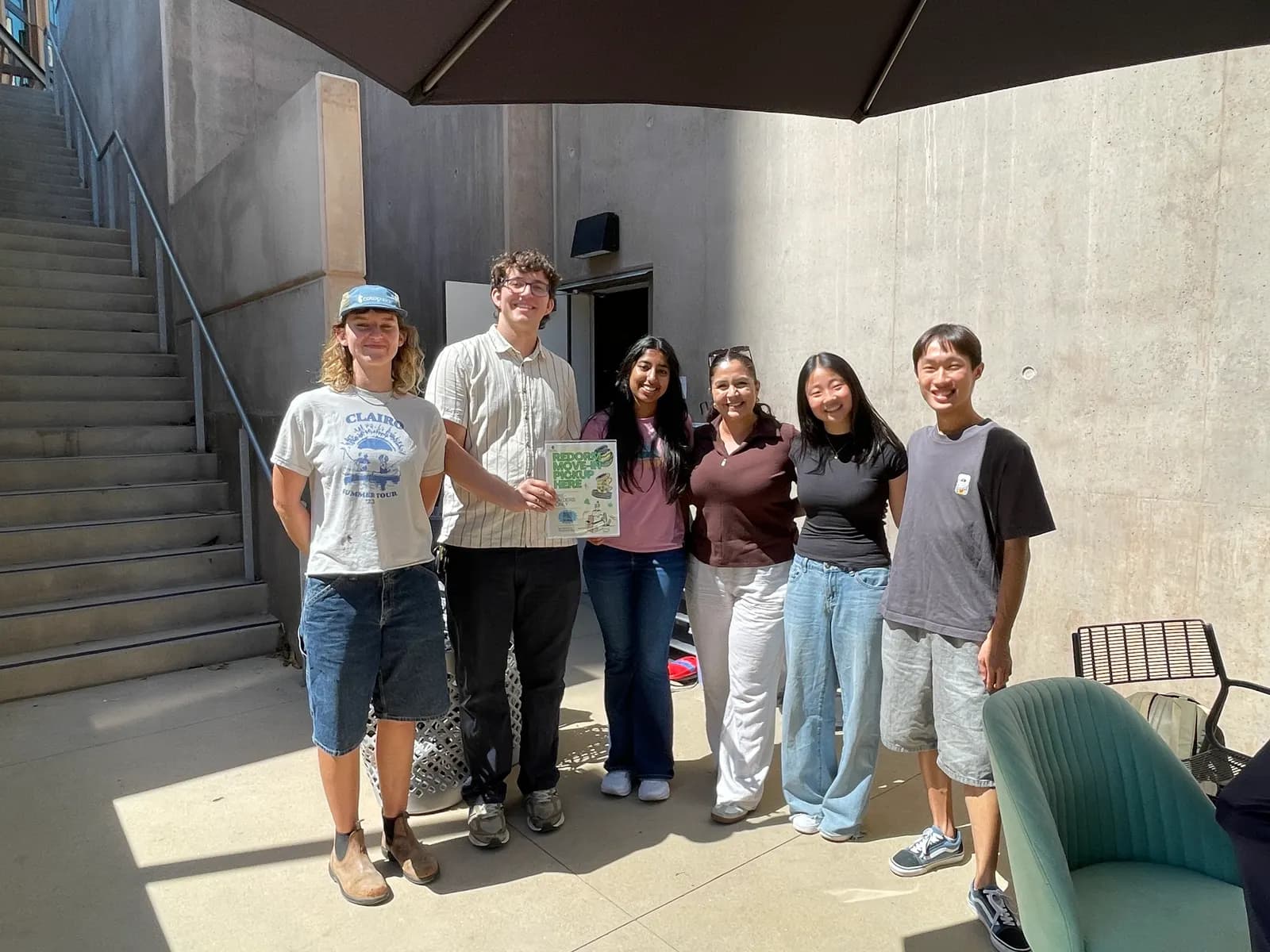 UC San Diego's move-in pickup team standing together in a concrete courtyard, one of them holding a ReDorm Move-In Pickup Here sign