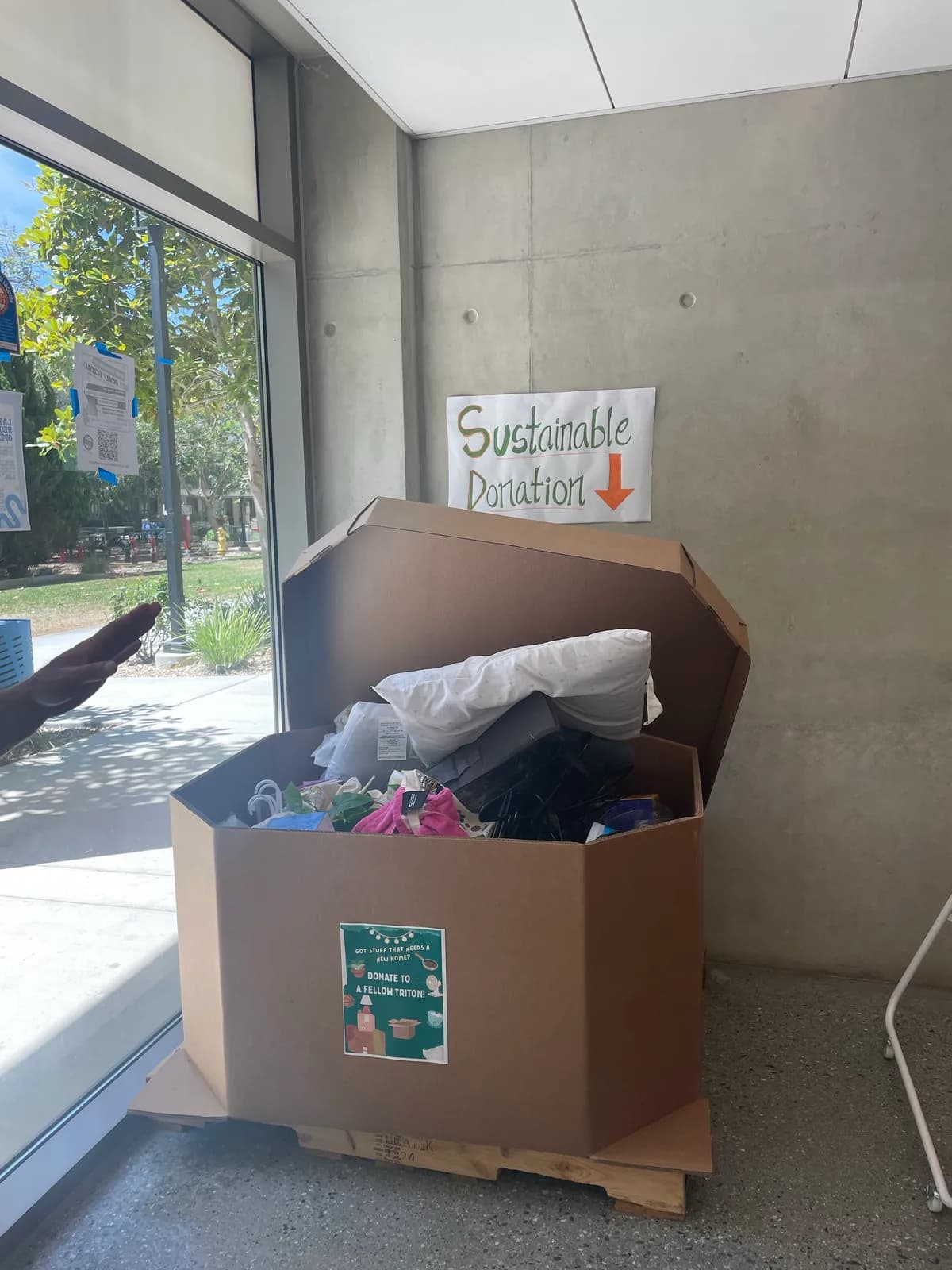 A large cardboard collection bin under a Sustainable Donation sign, filled with pillows and household goods