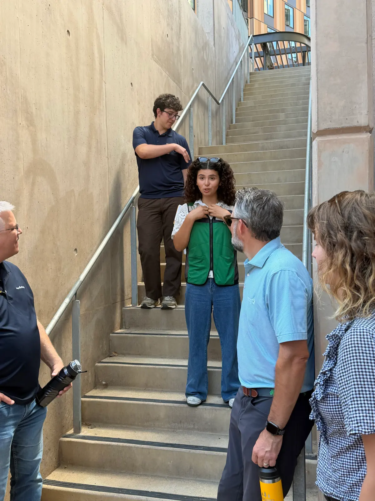 A person in a green ReDorm vest speaking with campus sustainability staff on an outdoor concrete stairwell between UC San Diego residence hall buildings